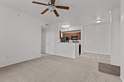 A room with a ceiling fan and a kitchenette in the background.