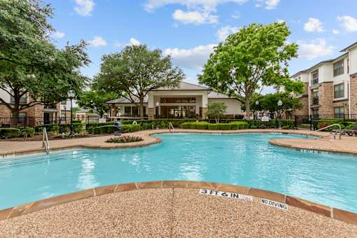 A pool surrounded by trees and a building in the background.