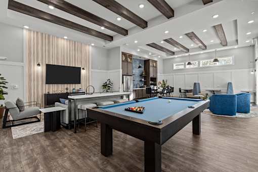 A pool table is in the middle of a room with a TV and a bar.