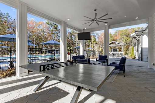 A table is in the middle of a patio with a pool and trees in the background.