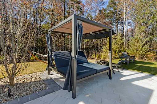 A grey and black outdoor daybed with a canopy is in the middle of a paved area.