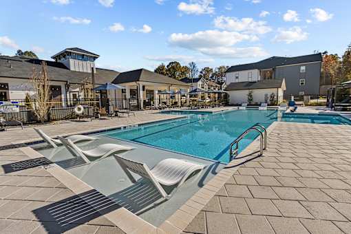 A large swimming pool with sun loungers and a building in the background.