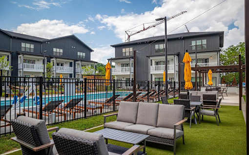 A poolside area with chairs, a sofa, and umbrellas in front of a building.