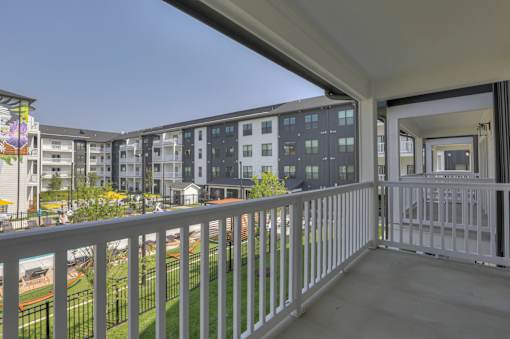 A balcony with a white railing overlooks a grassy area and buildings.