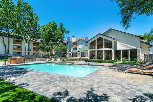 A swimming pool surrounded by a paved area and a few chairs.