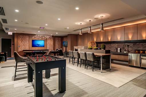 A modern room with a foosball table, bar stools, and a television.