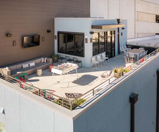 A patio with white chairs and a table is on the roof of a building.