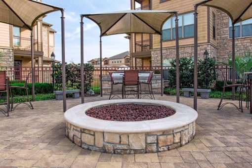 A patio with a fire pit and chairs under a canopy.