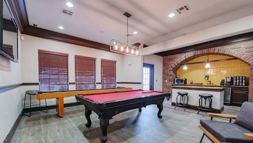 A pool table is in the middle of a room with a bar in the background.