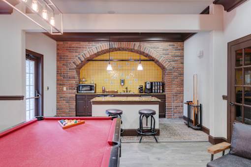 A pool table is in the middle of a room with a brick archway.