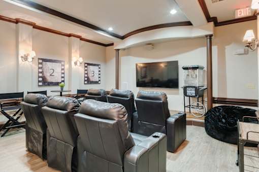 A row of black leather recliner chairs are lined up in a room with a large screen television.