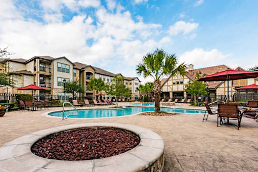 A pool surrounded by a patio with chairs and a fire pit.