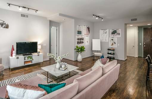 A living room with a pink couch and a television on a white cabinet.