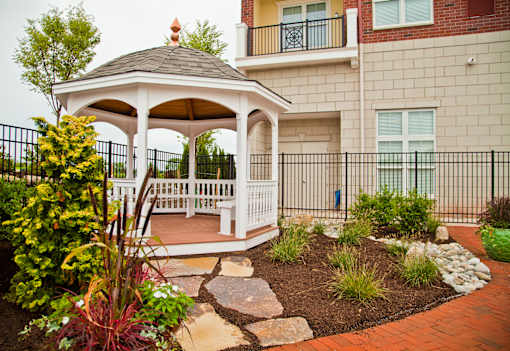 A gazebo is surrounded by a garden and a black fence.