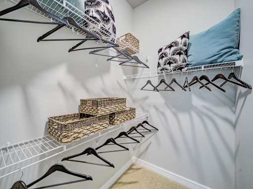 A white closet with clothes hanging and shelves with baskets.