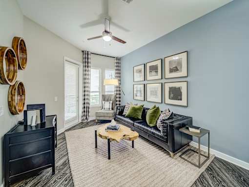 A living room with a black couch, a coffee table, and a ceiling fan.