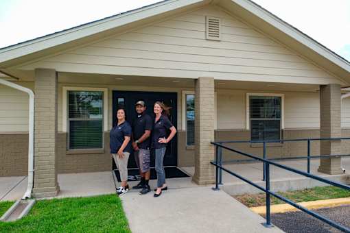 Four people in black shirts stand in front of a building.