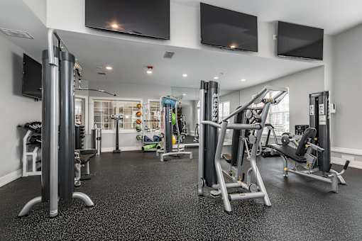 A spacious gym with various exercise equipment and flat screen TVs mounted on the wall.