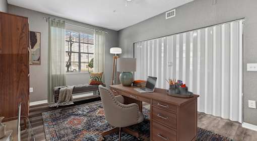 A room with a desk, chair, and a window with curtains.