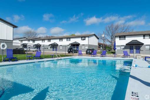 A swimming pool with blue chairs and a white building in the background.