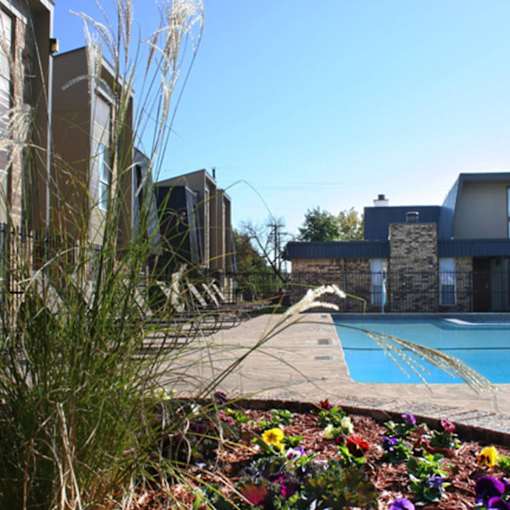 A pool surrounded by a flower bed and a building in the background.
