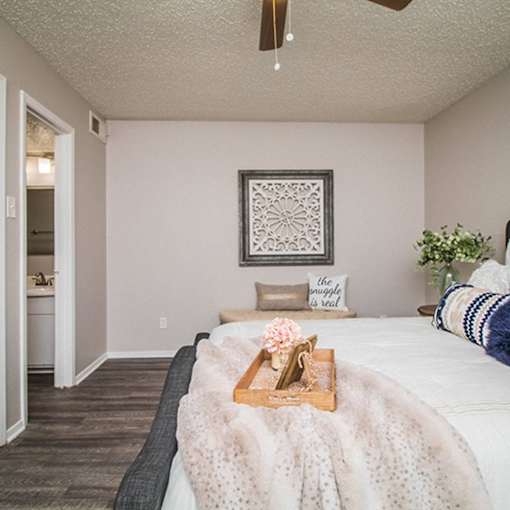 A bedroom with a bed covered in a white blanket and a wooden tray with flowers on it.