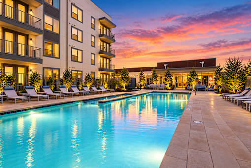 A large swimming pool is surrounded by lounge chairs in front of a building.