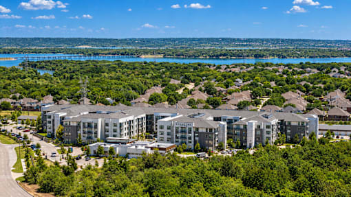 A large apartment complex is surrounded by trees and overlooks a large body of water.