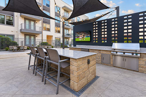 A patio with a bar and chairs under a black umbrella.