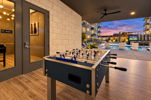 A foosball table is in the middle of a room with a pool table and a bar in the background.