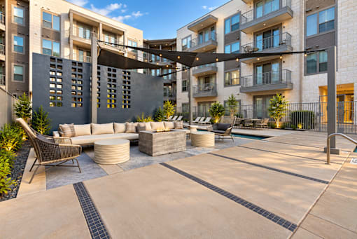 A modern outdoor seating area with a large table and chairs is surrounded by apartment buildings.
