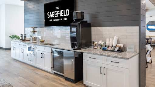 A kitchen area with a black fridge and a sign that says The Sage-field.