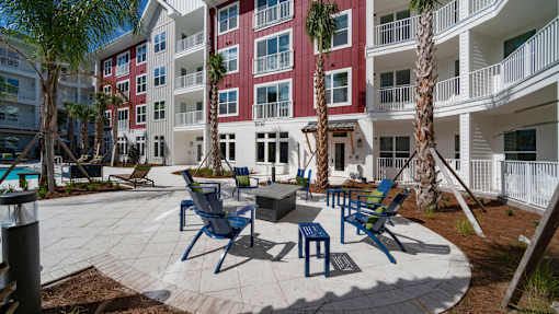 A patio area with chairs and tables in front of a red and white building.