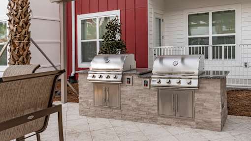 A red house with a white porch and a stone wall with a grill on it.