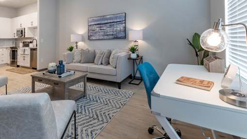 A modern living room with a grey couch, a coffee table, and a white desk.