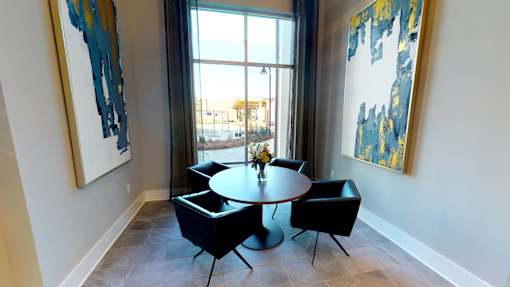 A round table with four chairs is in the middle of a room with two paintings on the wall.