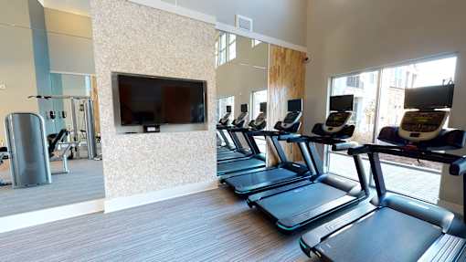A gym with treadmills and a television mounted on the wall.