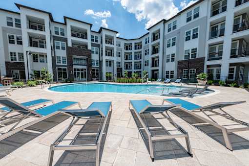 A pool surrounded by lounge chairs in front of apartment buildings.