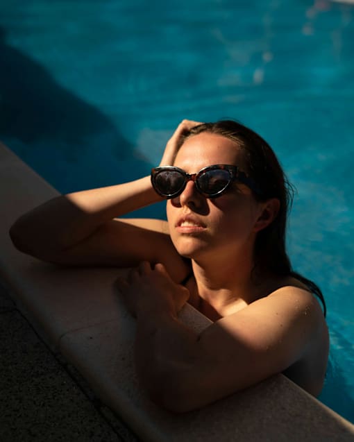 A person with sunglasses leaning on the edge of a pool.