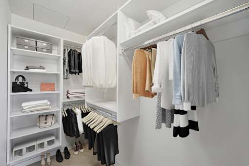 A white closet with clothes hanging and folded on shelves.