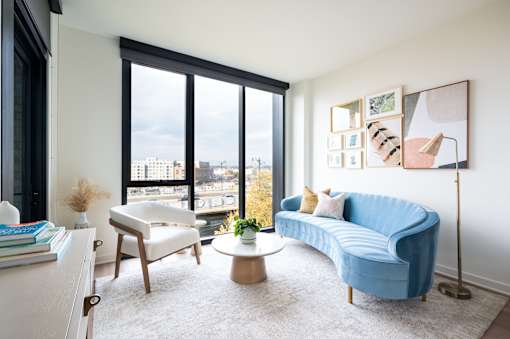 A blue couch sits in a living room with a large window overlooking the city.