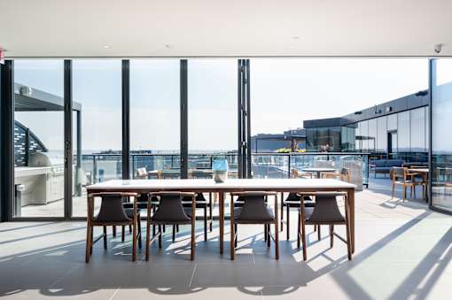 A long table with chairs is in a room with a glass wall.