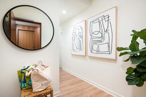 A room with a round mirror, a bag on a stool, and two framed artworks on the wall.