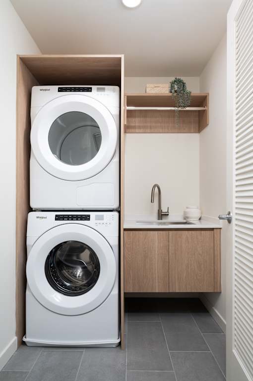 A white front loading washing machine is stacked on top of a smaller white one in a small laundry room.