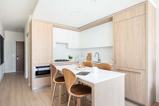 A modern kitchen with wooden chairs and a white counter.