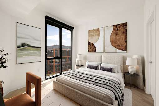 A bedroom with a large bed and a view of a cityscape through the window.