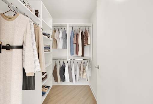 A white closet with clothes hanging on shelves and a beige sweater hanging on a hanger.