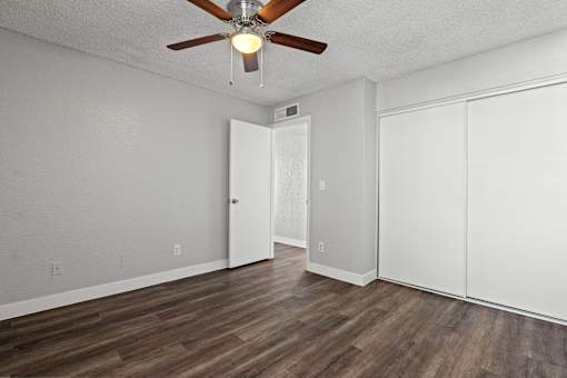 A room with a ceiling fan and wood flooring.