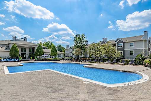A large swimming pool surrounded by a brick patio and lounge chairs.