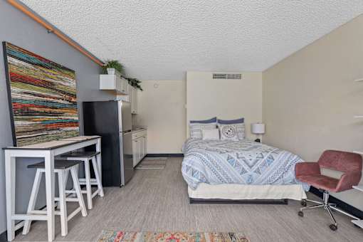 A bedroom with a bed, chair, and a fridge.